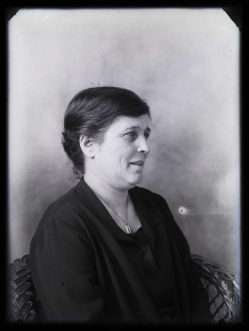 Portrait de femme, vue de 3/4 droit, assise dans un fauteuil, esquissant un sourire