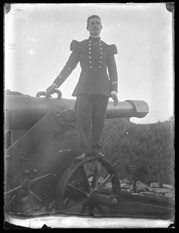Portrait d'un homme en tenue militaire d'apparat posant debout sur la roue d'un canon.