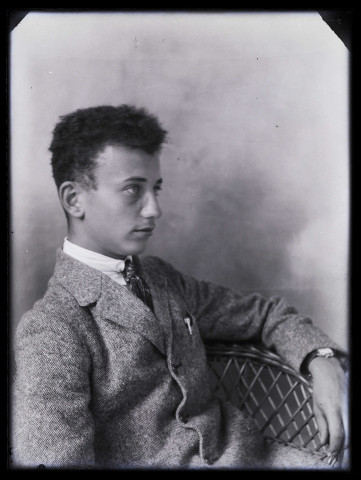 Portrait de jeune homme assis de 3/4 droit dans un fauteuil en rotin