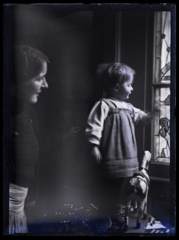 Louise Hertig et James regardant par la fenêtre en vitrail, un cheval de bois posé aux pieds de l'enfant