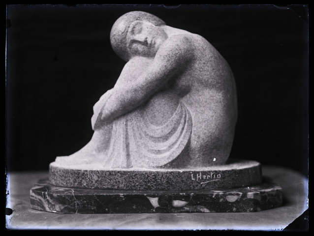 Groupe sculpté d'une femme assise, jambes repliées, la tête reposant sur ses genoux, photographiée dans l'atelier