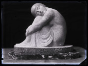 Groupe sculpté d'une femme assise, jambes repliées, la tête reposant sur ses genoux, photographiée dans l'atelier