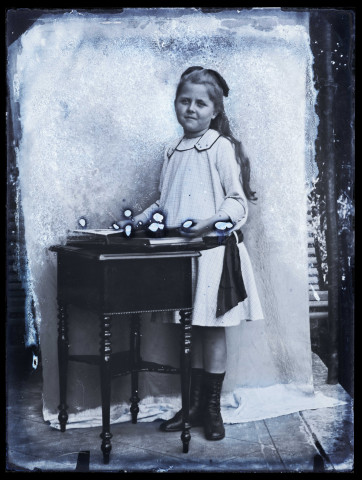 Fillette posant debout dans l'atelier, un livre ouvert posé sur un guéridon devant elle