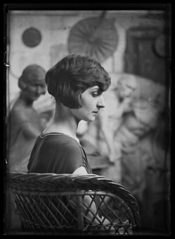 Jeune femme de profil (Andrée Cognard ?), assise dans un fauteuil en rotin, posant dans l'atelier de l'artiste