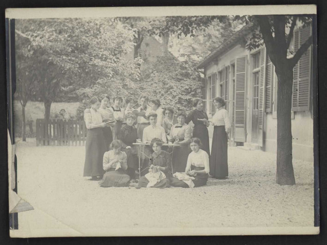 Personnel de l'école ménagère Jeanne d'Arc : photographie de groupe noir et blanc prise dans la cour devant les bâtiments [1912 environ].