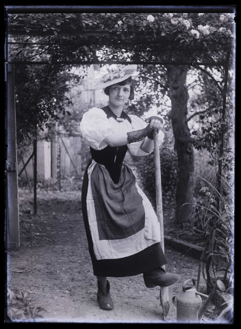 Jeune femme posant en jardinière, le pied sur une bêche, dans un jardin
