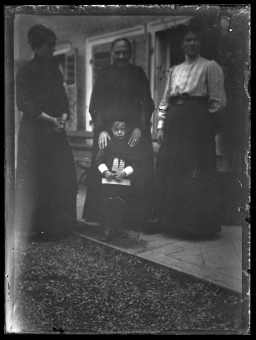 Trois femmes, dont Louise Hertig à gauche, posant debout devant la maison avec James Hertig enfant au centre